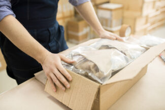 Close-up shot of male worker packing pressure sensors in cardboard box while working at warehouse of measuring equipment factory